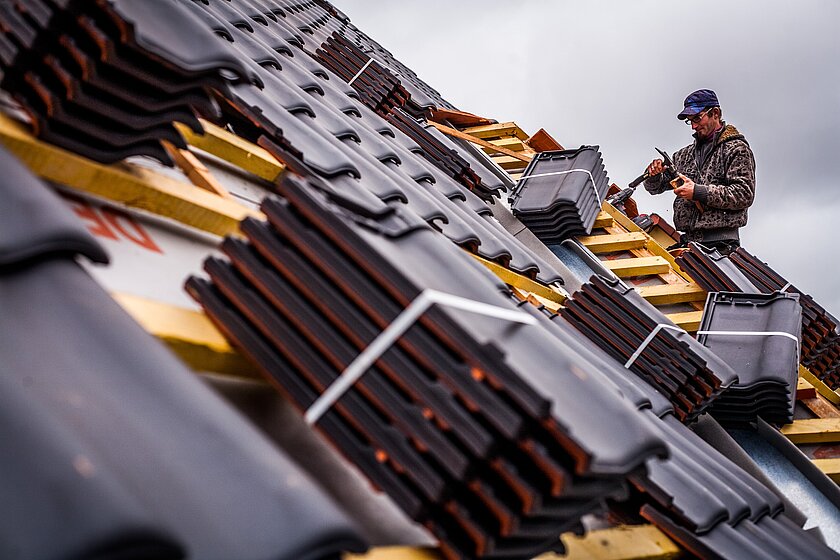 Dachdecker mit Ziegeln In der Bau- und Leistungsbeschreibung sollte alles so exakt wie möglich stehen, damit durch ungenaue Angaben keine geringere Qualität oder niedrigerer technischen Standard geliefert wird.