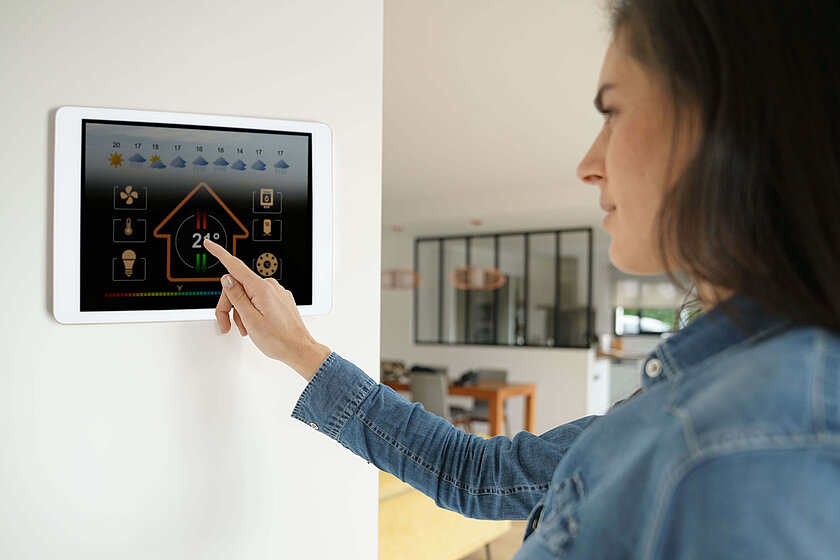 Eine Frau steuert gerade auf dem lokalen Bedienpanel ihres Smart Homes die Temperatur der Heizungsanlage.